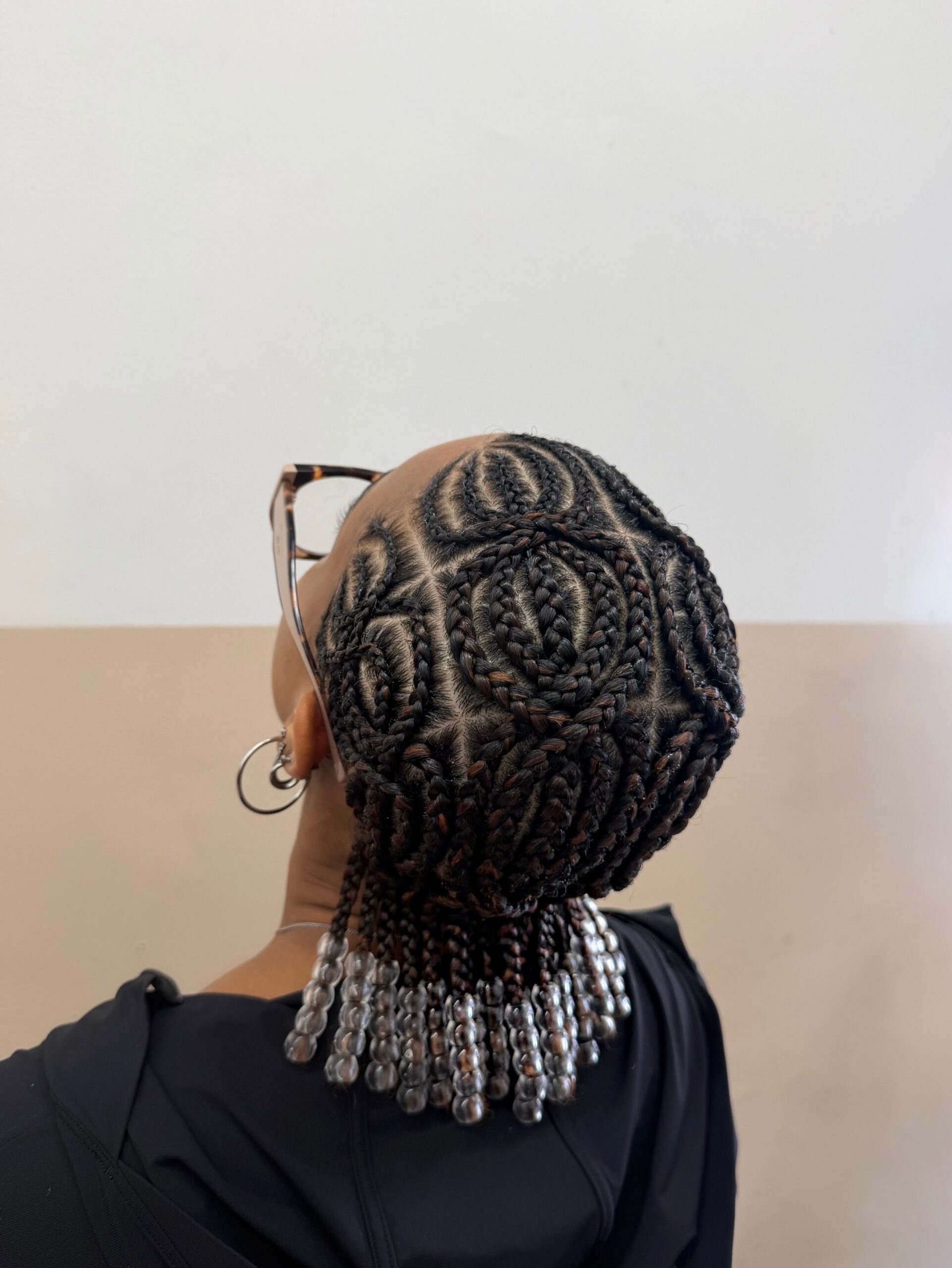 Short curved interwoven black and brown cornrow hairstyle with transparent beads.