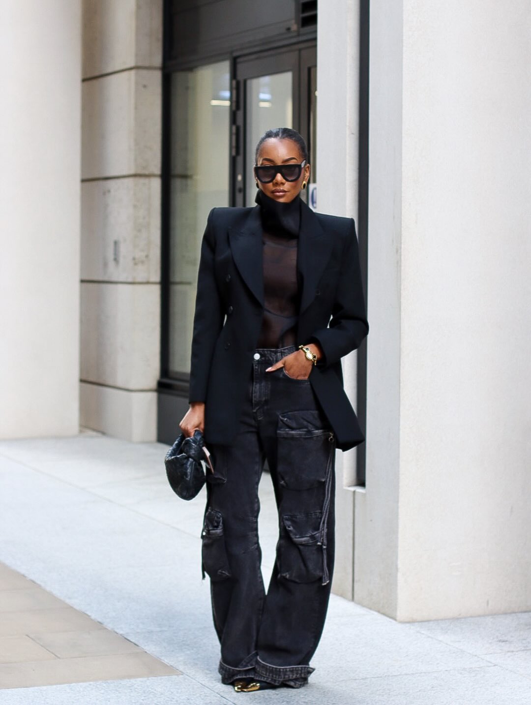 Minimalist street-style corporate outfit featuring a black double-breasted blazer and black straight-leg utility jeans.